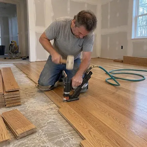 Installer nailing oak boards with pneumatic nailer during hardwood floor installation