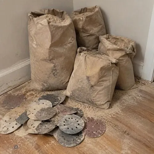 Sanding dust bags and used discs in corner during hardwood floor sanding and refinishing